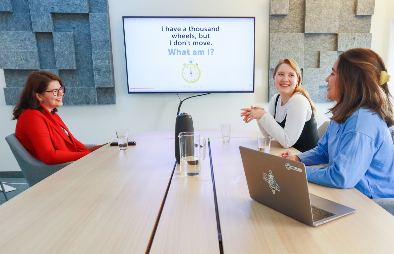 Three women having a discussion in a modern office with a presentation on screen.